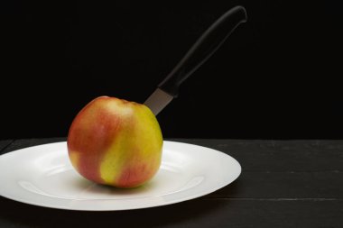 Elma siyah arkaplanda, bıçak beyaz tabakta.