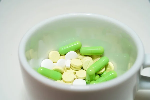 Bardaktaki haplar, yeşil haplar, tabletli büyük bir kupa, beyaz arka plandaki bardaktaki haplar.