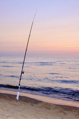 Gün batımında sahilde yalnız bir olta kamışı.