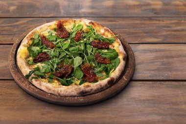 Arugula pizzası, ahşap bir masada kurutulmuş domates.