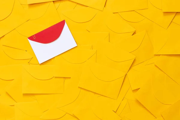 Masaya saçılmış sarı zarflar, beyaz bir kağıttaki yazı için boşluk ve işaretlenmiş kırmızı bir zarf. Üst görünüm.