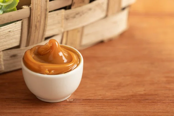 Dulce de leche beyaz bir kabın içinde tahta bir masanın üzerinde.