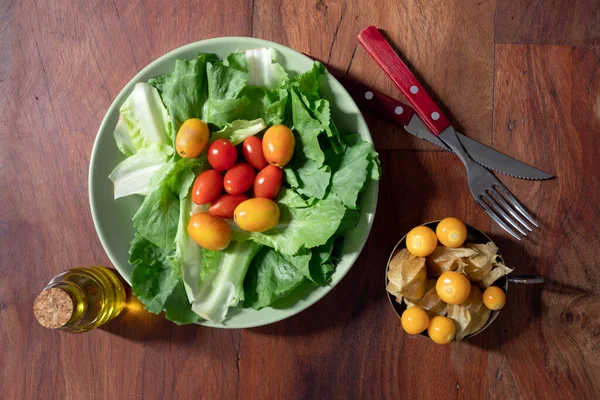 Bir tabak marul, kırmızı anne salatası ve yanında da fizsalis olan metal bir kap. Üst Görünüm