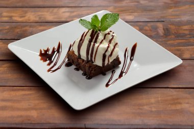 Kırsal bir masada, beyaz bir tabakta dondurmalı Brownie. Tatlı.