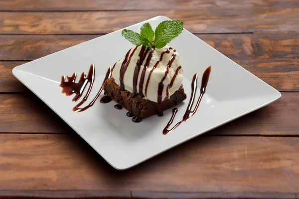 Kırsal bir masada, beyaz bir tabakta dondurmalı Brownie. Tatlı.