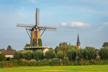 Geleneksel yel değirmeniyle tipik bir Hollanda manzarası. Kuzey Brabant, Terheijden köyündeki kilise kulesinin yanında.