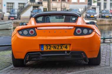 Amsterdam, Hollanda, 28.12.2025, 2011 yılından bu yana turuncu renkli ilk nesil batarya elektrikli spor otomobil Tesla Roadster 'ın arka görüntüsü
