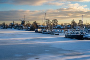 Weesp, Marina, Vecht nehri ve gün batımına kadar karla kaplı geleneksel yel değirmenlerinin kış manzarası.