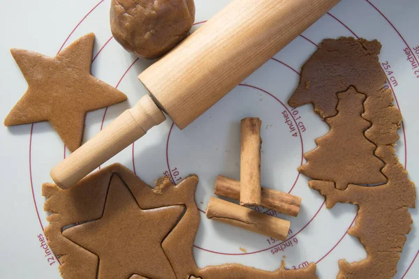 Ginger biscuit dough being cut into shapes on a pastry mat. Cinnamon sticks and rolling pin.