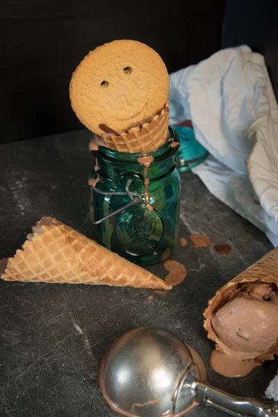 Melting chocolate ice cream, waffle cones, sugar cookie with a smiling face in a glass jar.