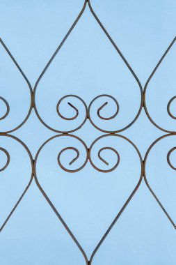 Rusty, curly, heart -shaped wrought iron gate on blue background. Opposites background