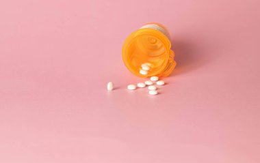 Turuncu plastik şişedeki oksikodon reçeteli ilaçların beyaz tabletleri pembe arka plana dökülüyor..