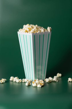 Patlamış mısırla dolu yeşil ve beyaz çizgili servis konteynırı koyu yeşil arka plana dökülüyor..