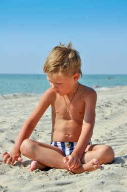 Çocuk kum deniz kenarında oturup...