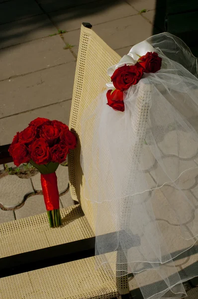 Schleier und ein Strauß roter Rosen liegen auf einem Stuhl — Stockfoto