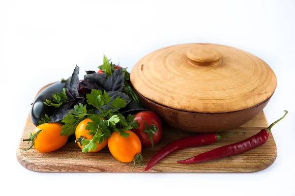 Vegetables and earthenware baking dish on a wooden board — Stock Photo, Image