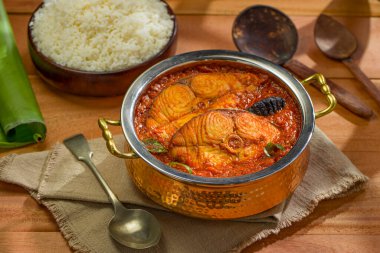 Kahin Balık köri, geleneksel Hint balık körisi, kerala spesiyali, bir kase pilav ve muz yaprağıyla birlikte servis edilen bakır servis kasesinde, ahşap desenli arka planda, izole edilmiş..
