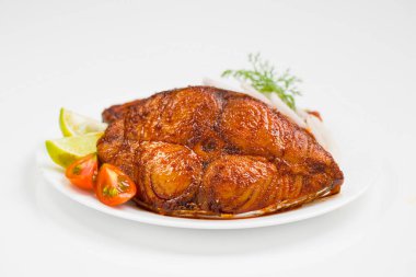 Kahin balık kızartması, beyaz seramik tabakta soğan, limon ve domates dilimleriyle süslenmiş, beyaz desenli arka planda güzelce düzenlenmiş..