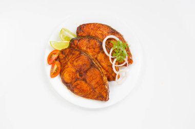 Kahin balık kızartması, beyaz seramik tabakta soğan, limon ve domates dilimleriyle süslenmiş, beyaz desenli arka planda güzelce düzenlenmiş..