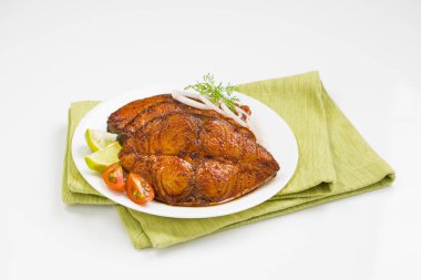 Kahin balık kızartması soğan, limon ve domates dilimleriyle süslenmiş yeşil peçeteye yerleştirilmiş beyaz desenli arkaplan..