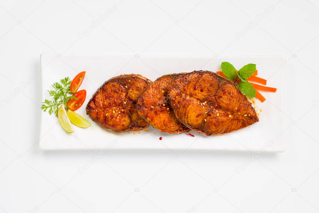 Seer fish fry arranged beautifully and garnished with onion, lemon and tomato slices on white rectangle shape ceramic plate placed on white textured background.