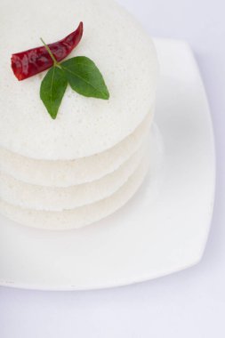 Idly ya da Idli, Güney Hindistan ana kahvaltı öğesi kırmızı kuru acı biber ve köri yapraklarıyla süslenmiş beyaz arka planda güzelce düzenlenmiş, izole edilmiş, yakın plan ve üst manzara.