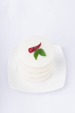 Idly ya da Idli, Güney Hindistan ana kahvaltı öğesi kırmızı kuru acı biber ve köri yapraklarıyla süslenmiş beyaz arka planda güzelce düzenlenmiş, izole edilmiş, yakın plan ve üst manzara.