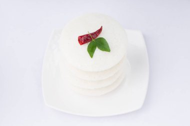Idly ya da Idli, Güney Hindistan ana kahvaltı öğesi kırmızı kuru acı biber ve köri yapraklarıyla süslenmiş beyaz arka planda güzelce düzenlenmiş, izole edilmiş, yakın plan ve üst manzara.