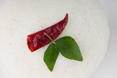 Idly ya da Idli, Güney Hindistan ana kahvaltı öğesi kırmızı kuru acı biber ve köri yapraklarıyla süslenmiş beyaz arka planda güzelce düzenlenmiş, izole edilmiş, yakın plan ve üst manzara.