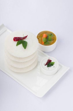 Idli ya da garnitürlü, Hint ana kahvaltı öğesi kırmızı acı biber ve köri yapraklarıyla süslenmiş beyaz dikdörtgen tabanlı, iki küçük kase sambar ve beyaz desenli arkaplamalı turşu ile güzelce düzenlenmiş..