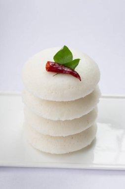 Idly ya da Idli, kırmızı acı biber ve köri yapraklarıyla süslenmiş Güney Hindistan ana kahvaltı öğesi beyaz desenli arka planda beyaz dikdörtgen üzerine güzelce yerleştirilmiş..
