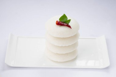 Idly ya da Idli, kırmızı acı biber ve köri yapraklarıyla süslenmiş Güney Hindistan ana kahvaltı öğesi beyaz desenli arka planda beyaz dikdörtgen üzerine güzelce yerleştirilmiş..
