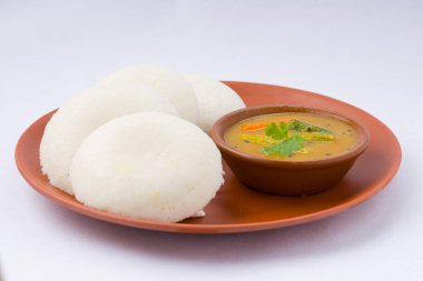 Idly ya da Idli, Güney Hindistan ana kahvaltı öğesi. Beyaz arka planda küçük bir kase sambar ile toprakta güzelce düzenlenmiş..