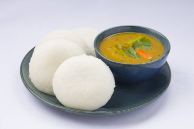 Idly ya da Idli, Güney Hindistan ana kahvaltı öğesi. Beyaz arka planda küçük bir kase sambar ile güzel bir şekilde düzenlenmiş..