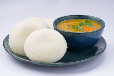 Idly ya da Idli, Güney Hindistan ana kahvaltı öğesi. Beyaz arka planda küçük bir kase sambar ile güzel bir şekilde düzenlenmiş..