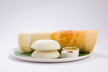 Ghee rosto Dosa ve Idlii, Güney Hindistan ana kahvaltı öğesi. Beyaz arka planda muz yaprağı ve köri ile kaplı beyaz bir tabakta güzelce düzenlenmiş..