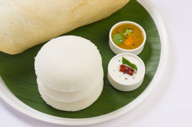 Ghee rosto Dosa ve Idlii, Güney Hindistan ana kahvaltı öğesi. Beyaz arka planda muz yaprağı ve köri ile kaplı beyaz bir tabakta güzelce düzenlenmiş..