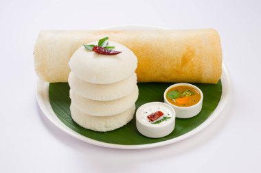 Ghee rosto Dosa ve Idlii, Güney Hindistan ana kahvaltı öğesi. Beyaz arka planda muz yaprağı ve köri ile kaplı beyaz bir tabakta güzelce düzenlenmiş..