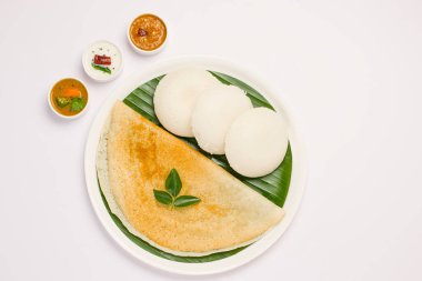 Ghee rosto Dosa ve Idlii, Güney Hindistan ana kahvaltı öğesi. Beyaz arka planda muz yaprağı ve köri ile kaplı beyaz bir tabakta güzelce düzenlenmiş..