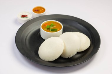 Idly ya da Idli, Güney Hindistan ana kahvaltı öğesi beyaz arka planda siyah bir tabakta güzelce düzenlenmiştir..