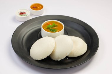 Idly ya da Idli, Güney Hindistan ana kahvaltı öğesi beyaz arka planda siyah bir tabakta güzelce düzenlenmiştir..