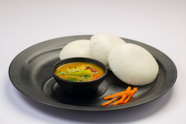Idly ya da Idli, Güney Hindistan ana kahvaltı öğesi beyaz arka planda siyah bir tabakta güzelce düzenlenmiştir..