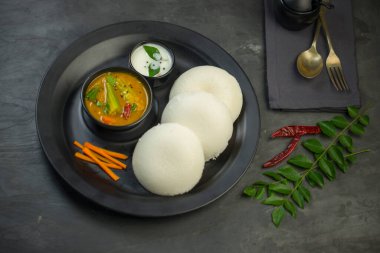 Idly ya da Idli, Güney Hindistan ana kahvaltı öğesi. Mutfak arka planında gri desenli siyah bir tabakta güzelce düzenlenmiş..