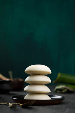 Idly ya da Idli, Güney Hindistan ana kahvaltı öğesi bir yığın üzerine yerleştirilir güzel bir şekilde siyah bir tabakta yerleştirilmiş mutfak arka planı ile koyu yeşil doku, seçici odaklı.