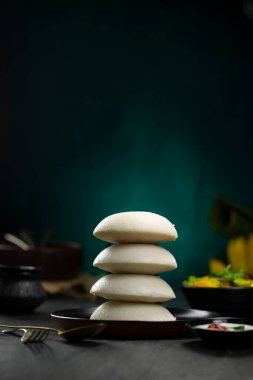 Idly ya da Idli, Güney Hindistan ana kahvaltı öğesi bir yığın üzerine yerleştirilir güzel bir şekilde siyah bir tabakta yerleştirilmiş mutfak arka planı ile koyu yeşil doku, seçici odaklı.
