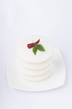 Idly ya da Idli, Güney Hindistan ana kahvaltı öğesi kırmızı kuru acı biber ve köri yapraklarıyla süslenmiş beyaz arka planda güzelce düzenlenmiş, izole edilmiş, yakın plan ve üst manzara.