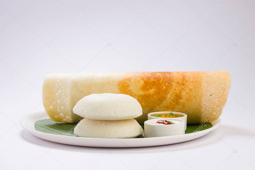 Ghee roast  Dosa and Idlii, south indian main breakfast item which is beautifully arranged in a white plate lined with banana leaf  and curry as sambar and chutney on white background.