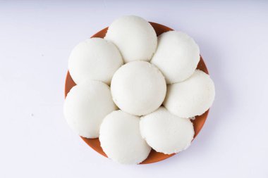 Idly ya da Idli, Güney Hindistan 'ın ana kahvaltı malzemesi. Beyaz arka planda, toprak tabakasında güzelce düzenlenmiş..