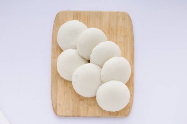 Idly ya da Idli, Güney Hindistan ana kahvaltı öğesi. Beyaz arka planlı, ahşap bir zeminde güzelce düzenlenmiş..