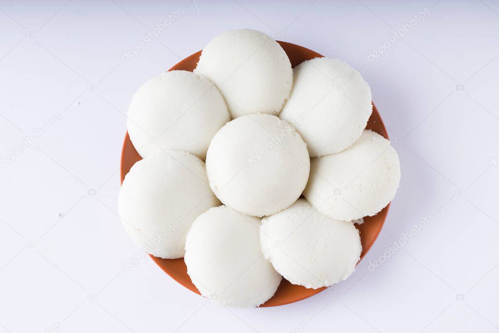 Idly or Idli, south indian main breakfast item which is beautifully arranged in an earthen ware with  white background.